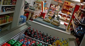 Ein Supermarkt mit Regalen voller verschiedener Produkte, einer Kasse und einer Person im Hintergrund.