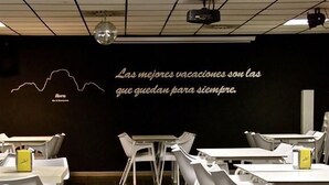 Een restaurantinterieur met witte tafels en stoelen, een zwarte muur met een citaat, en een discobal.