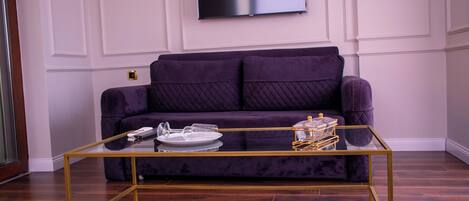 Ein Wohnzimmer mit einem violetten Sofa, einem Glastisch und einem flachbildfernseher an der Wand.