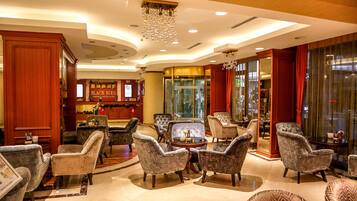 A lobby with a reception desk, seating area with armchairs and a coffee table, and a large chandelier.