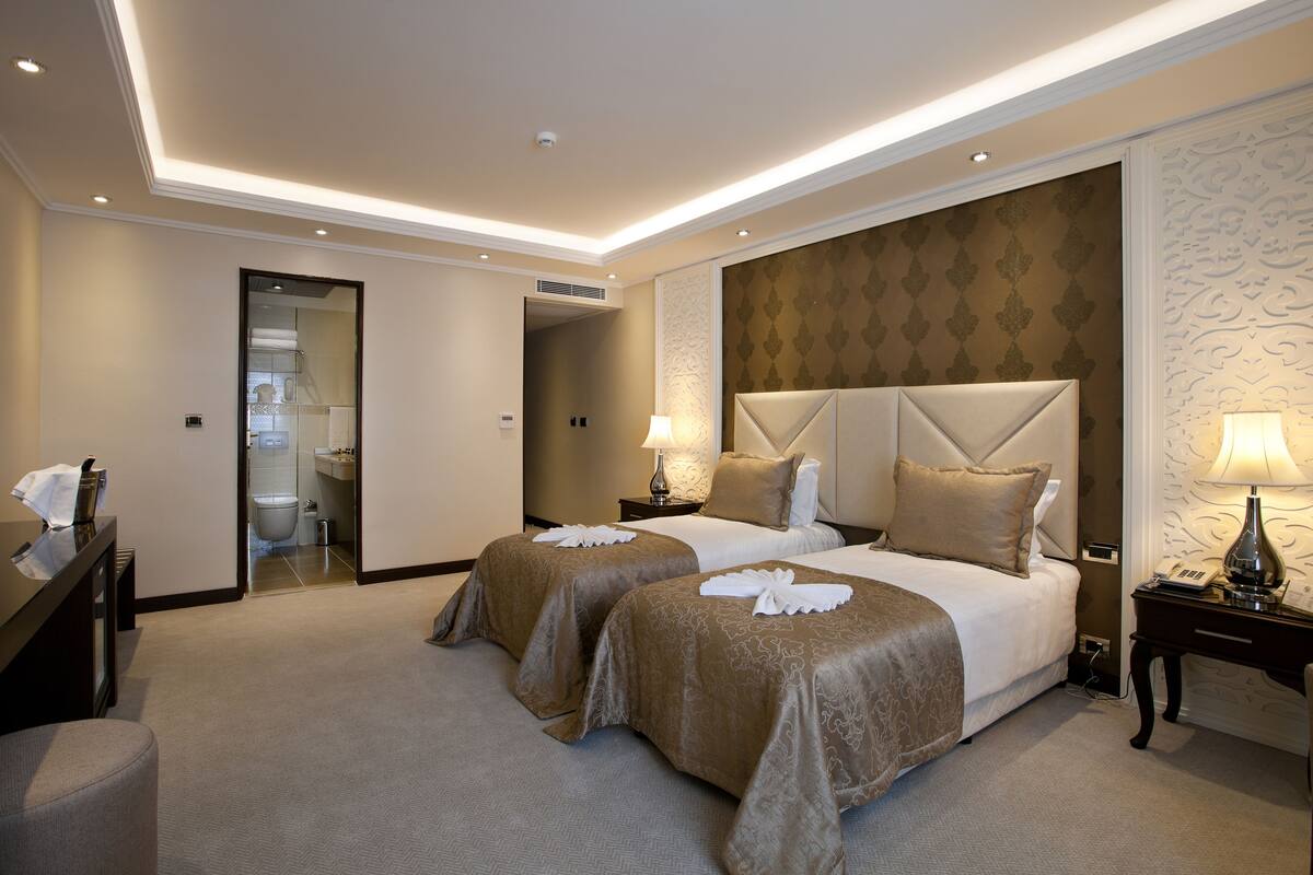 A hotel room with two beds, a desk, and a bathroom visible through an open door.