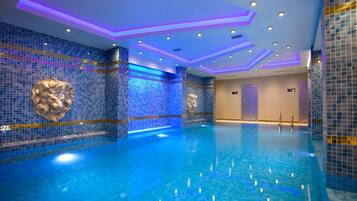 A modern indoor swimming pool with blue mosaic tiles and decorative lion head sculptures.