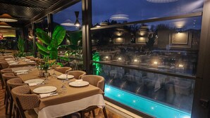 A restaurant with tables set for dining, large windows with a view of the pool, and indoor plants. - Black Bird Thermal Hotel & Spa (Termal)