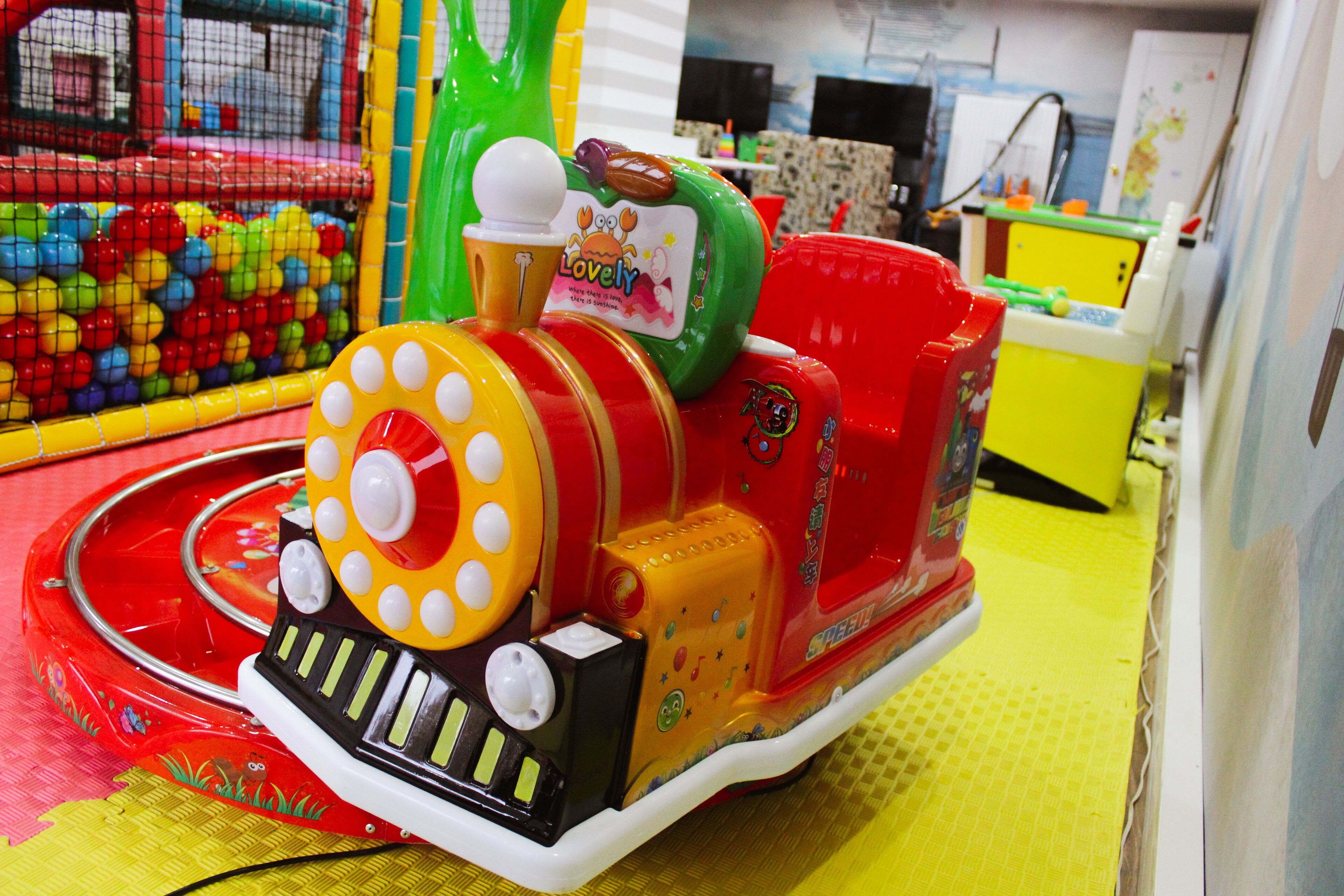 A colorful children's ride with a train theme, including a red and yellow locomotive and a green car.