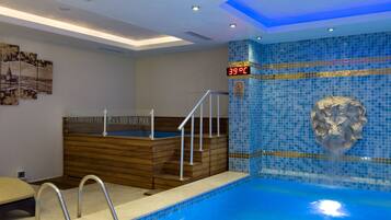 A swimming pool with a wooden hot tub, a lion head mosaic, and a temperature display.