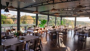 An indoor dining area with tables and chairs, large windows, and hanging pendant lights. - Black Bird Thermal Hotel & Spa (Termal)