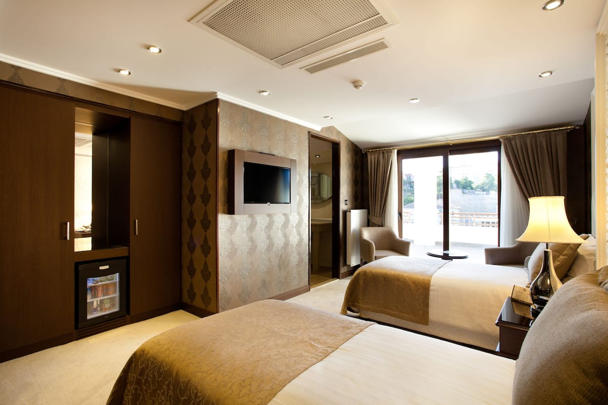 A hotel room with two beds, a television, a minibar, and a large window with curtains.