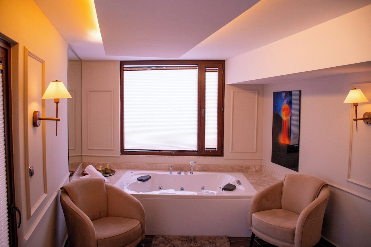 A bathroom with a large bathtub, two chairs, and a painting on the wall.