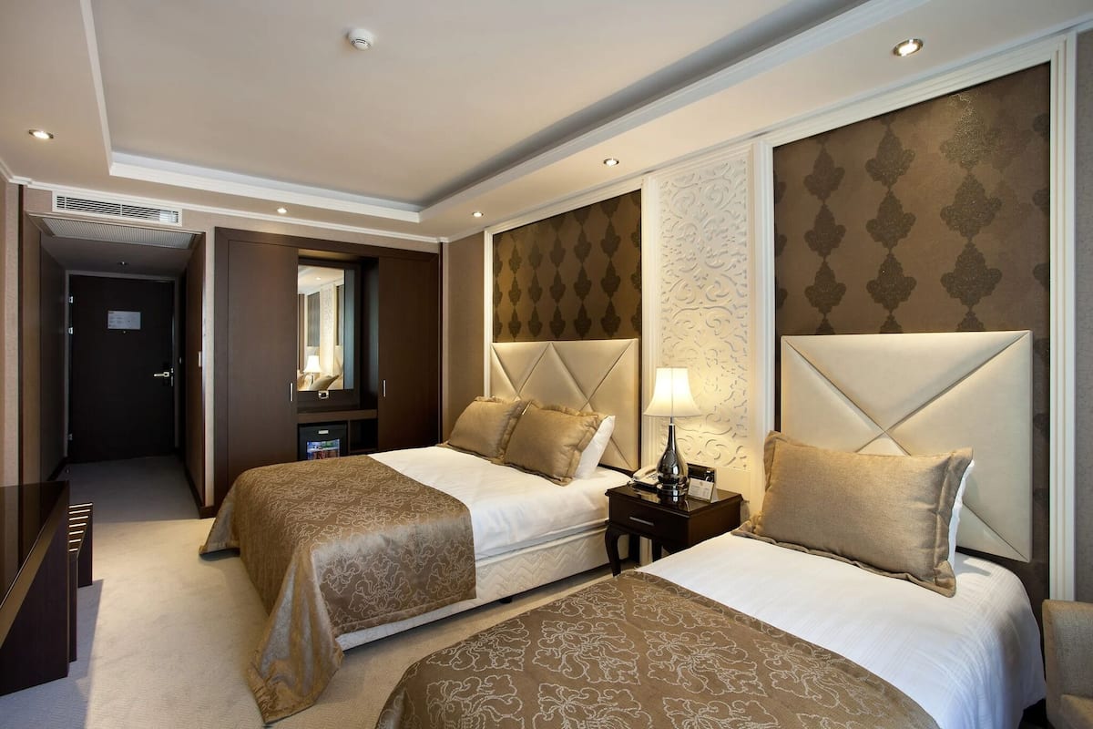 A hotel room with two beds, a mirror, a nightstand, and a wall with a patterned design.