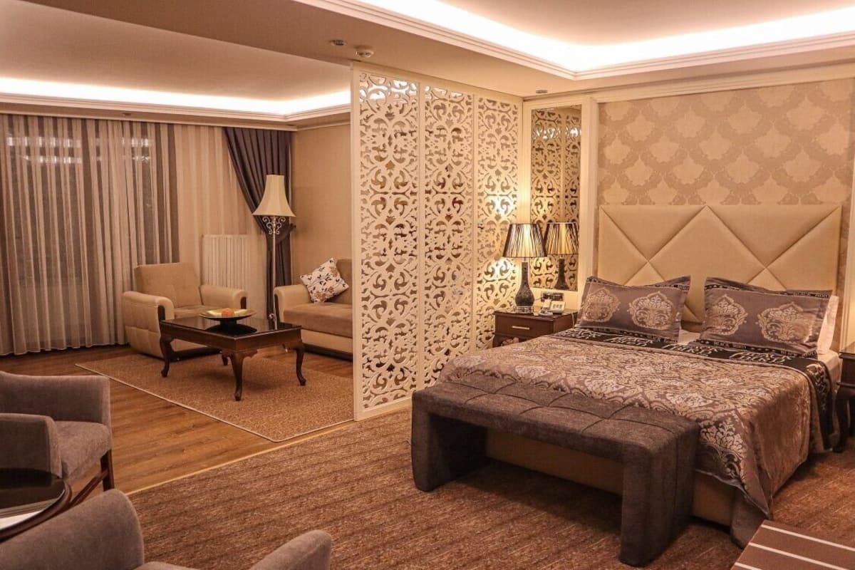 A hotel room with a large bed, a sofa, a coffee table, and a decorative partition.