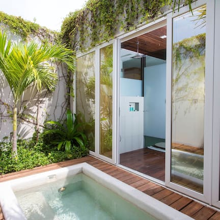 A modern outdoor pool area with a wooden deck, surrounded by lush greenery and a glass-enclosed space.