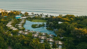 Vista aérea de un resort con una piscina grande, varias villas y vista al océano.