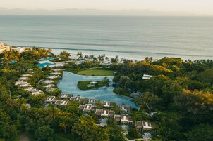 Vista aérea de un resort con una piscina grande, varias villas y vista al océano.