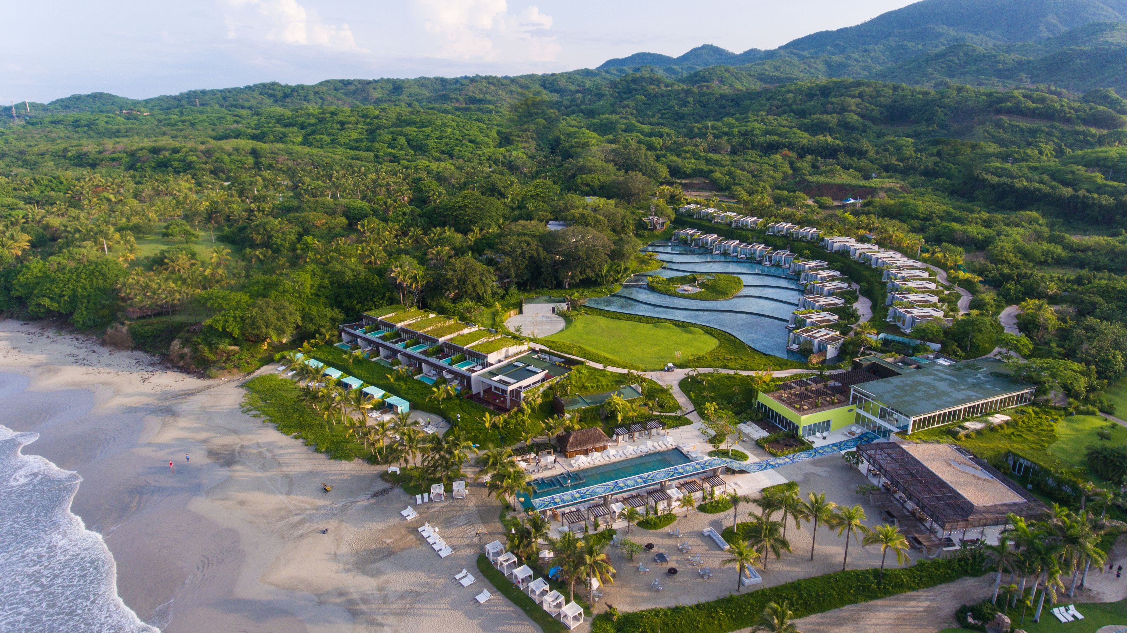 Vue aérienne d’un complexe hôtelier comprenant plusieurs bâtiments, une piscine et une plage.
