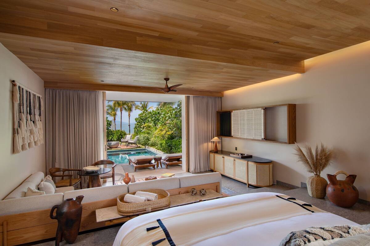 Un dormitorio amplio con una cama grande, una zona de estar con vista a la piscina y un televisor montado en la pared.