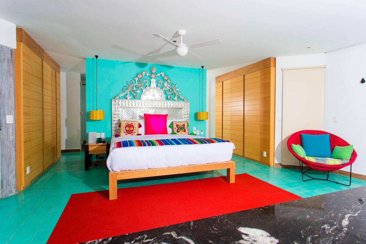 Un dormitorio con cama, una silla roja, ventilador de techo y armarios de madera.
