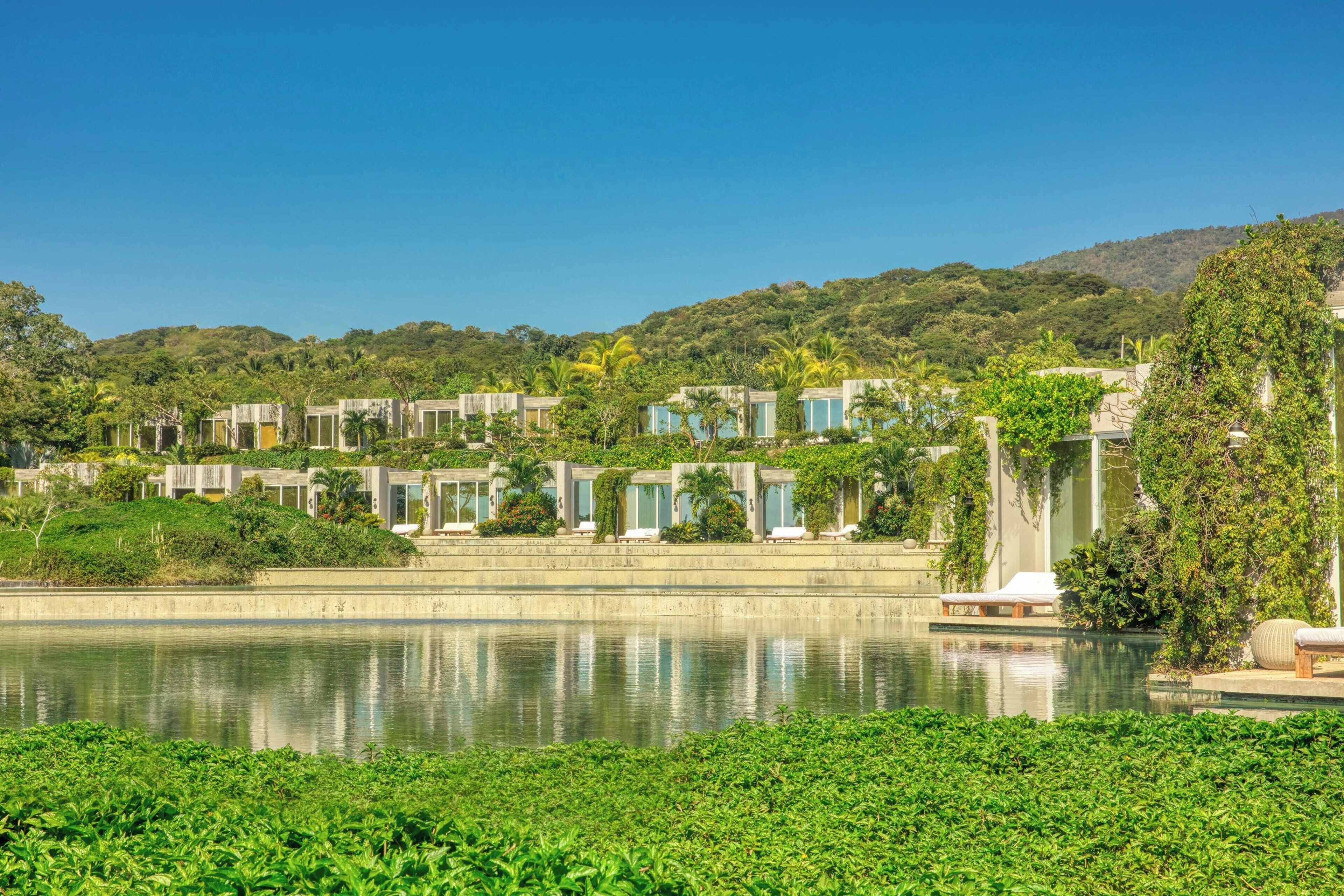 A resort with multiple villas along a lake, surrounded by lush greenery and hills.