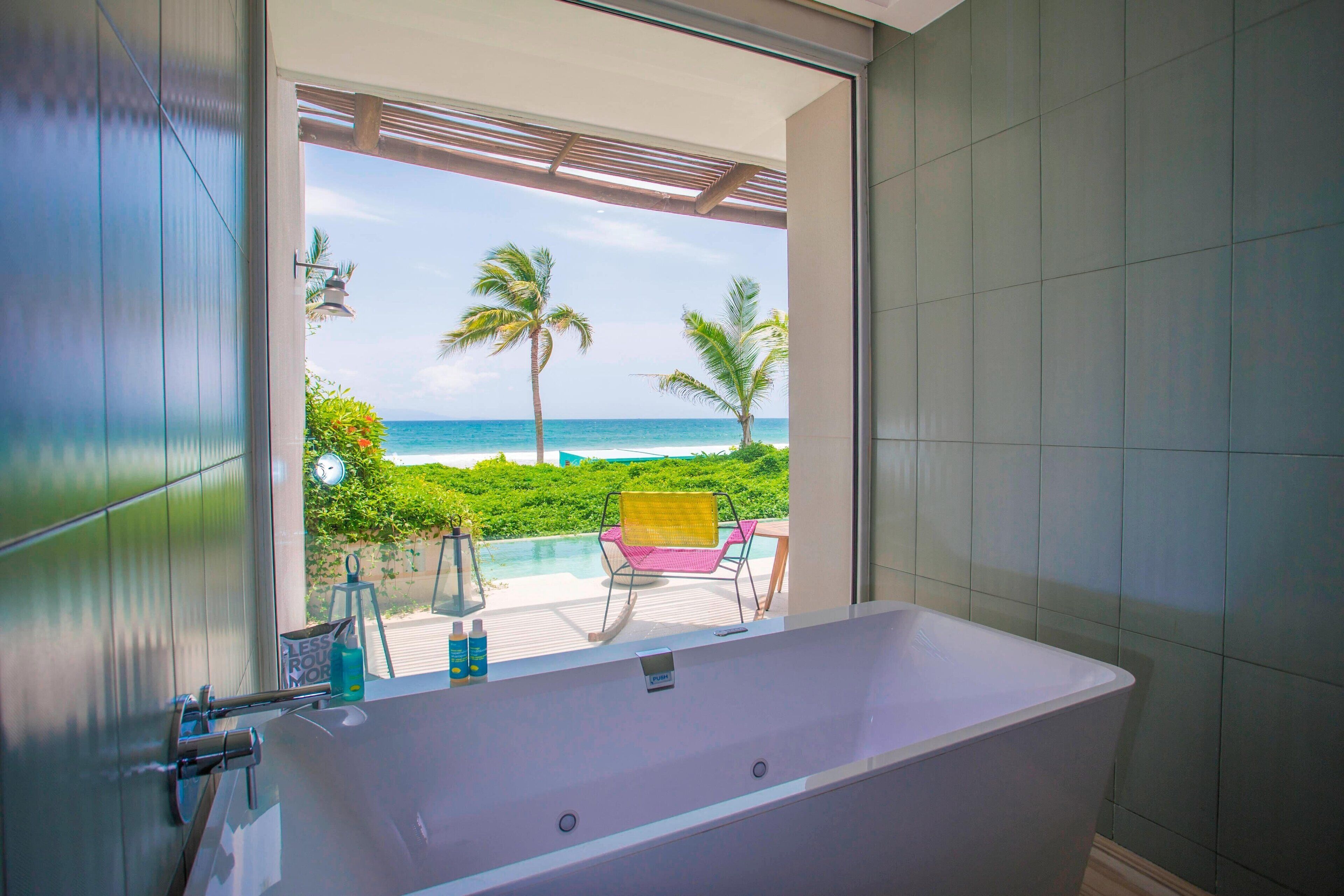 A bathroom with a large bathtub, a view of the ocean, and a chair outside.