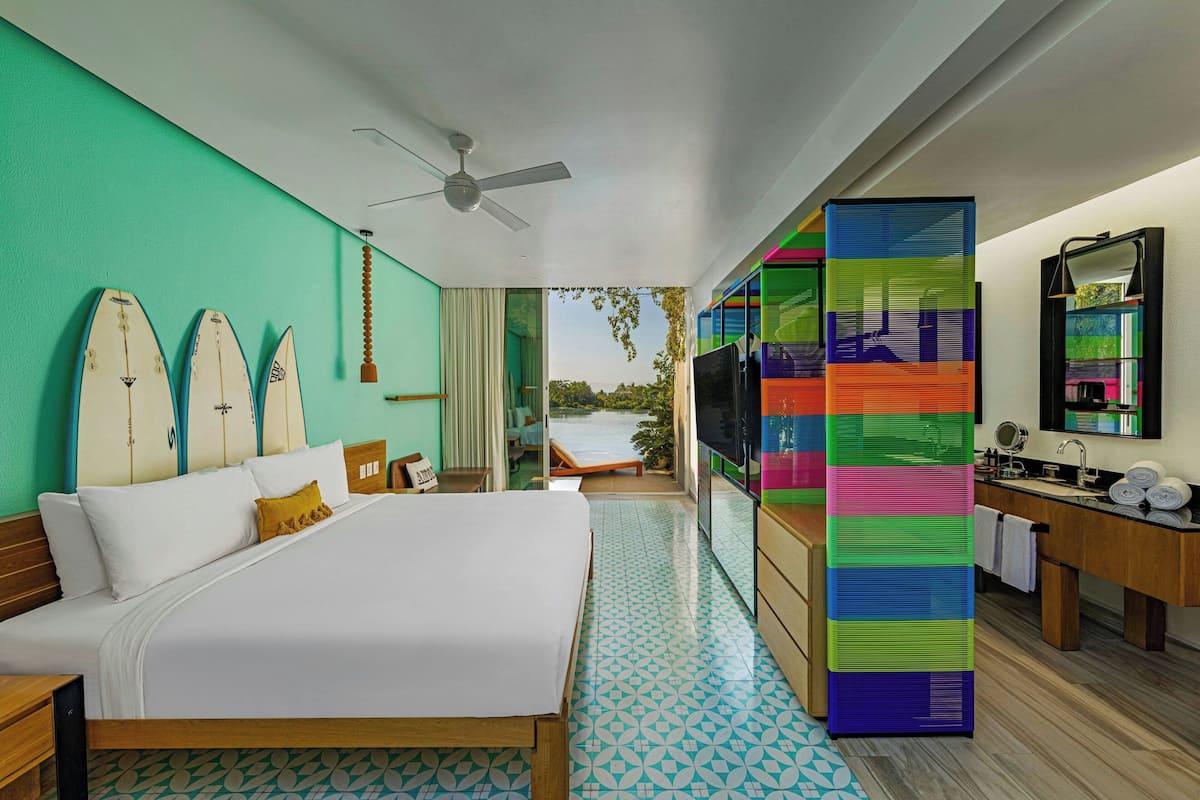 Habitación de hotel con una cama, televisión, baño con espejo y tablas de surf en la pared.