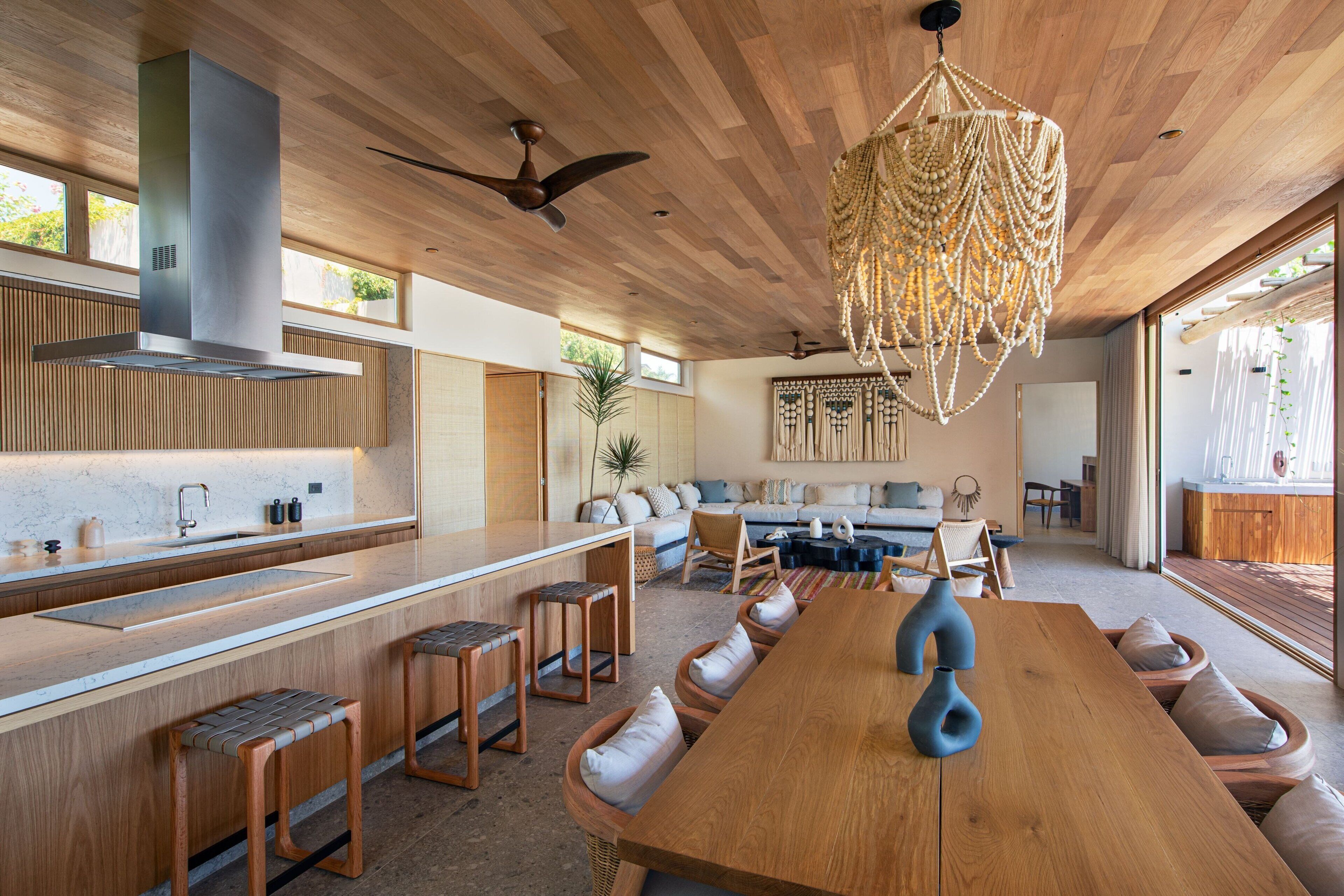 A modern kitchen with a wooden countertop, bar stools, and a large dining table.