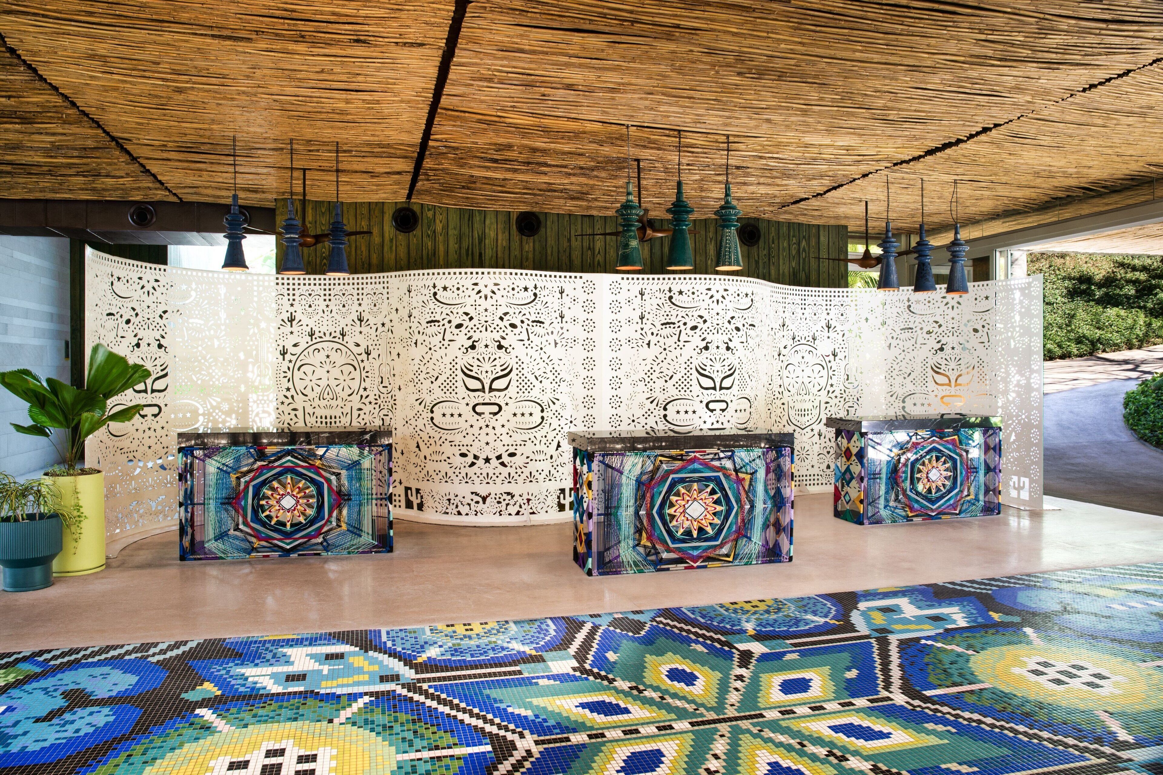 A room with a woven ceiling, a decorative partition with intricate patterns, and three colorful, patterned side tables.