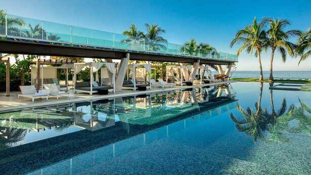 Una piscina cristalina con sillones de descanso y un puente de cristal con vistas al mar.