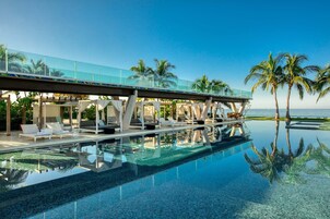 Una piscina cristalina con sillones de descanso y un puente de cristal con vistas al mar.