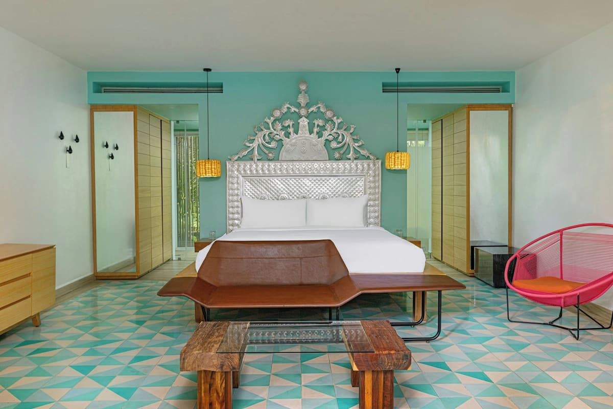 Un dormitorio con una cama, un banco de madera, una silla rosa y un suelo con estampado.