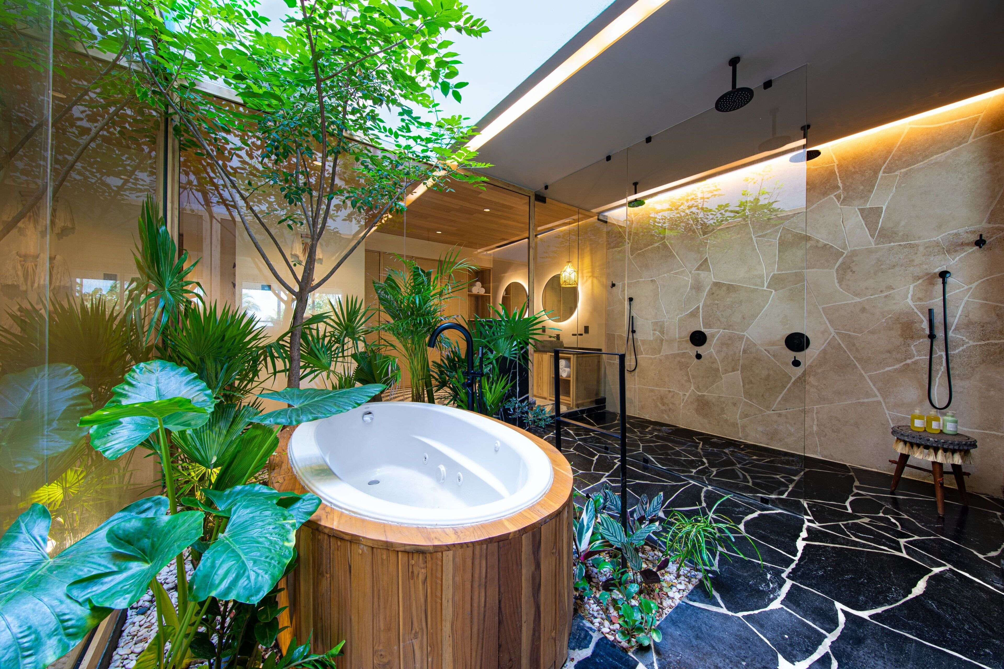 A modern bathroom with a stone floor, a wooden bathtub, and various plants.