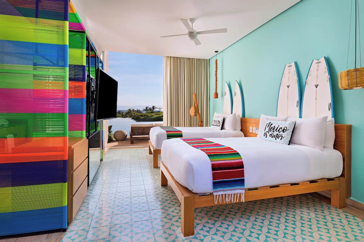 Habitación de hotel con dos camas, televisor y balcón con vista al océano.