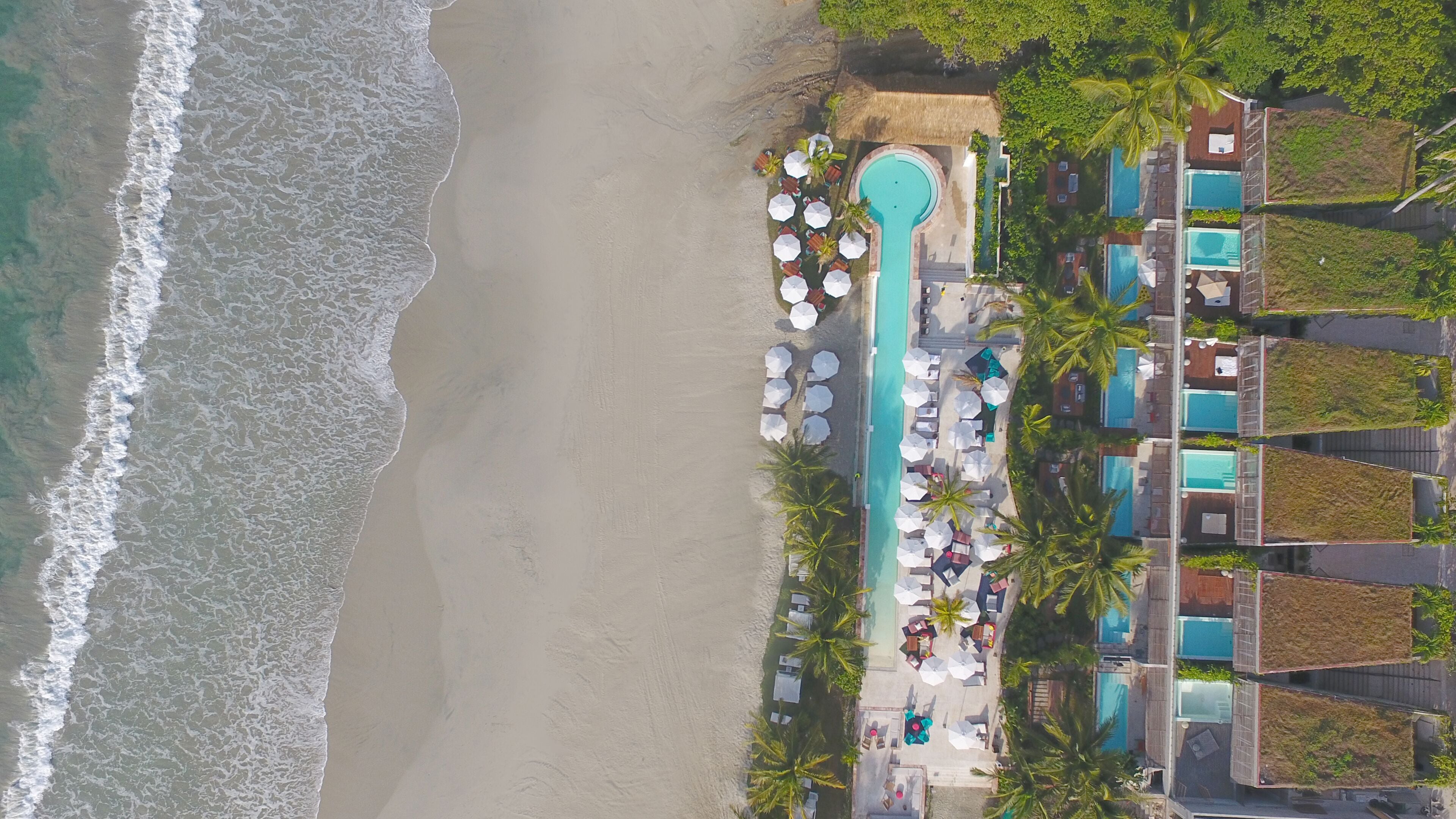 Een overzicht vanuit de lucht van een resort met een strand, een zwembad en meerdere gastenkamers.