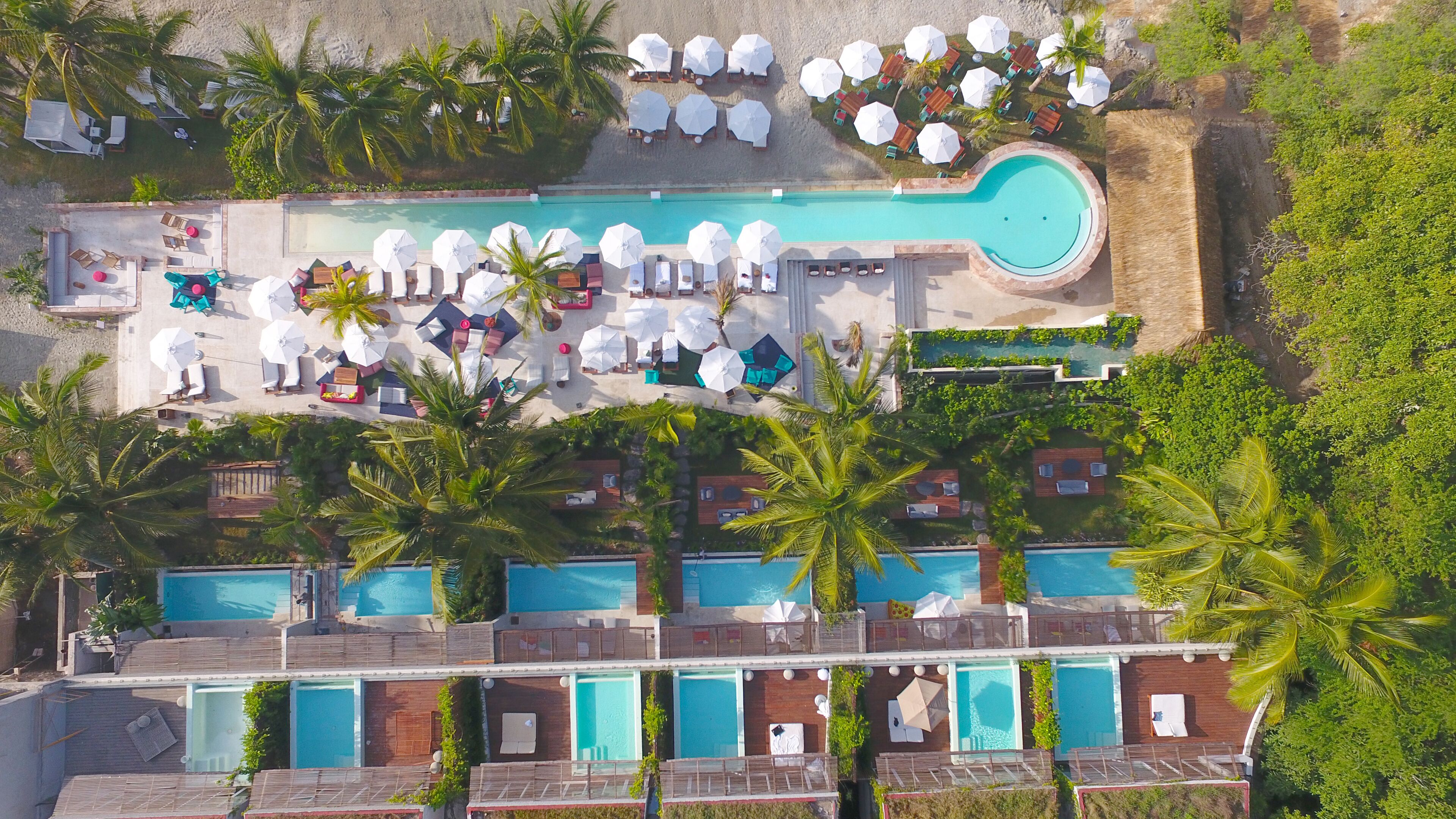 Vue aérienne d’un complexe hôtelier doté de plusieurs piscines, de chaises longues et de parasols.