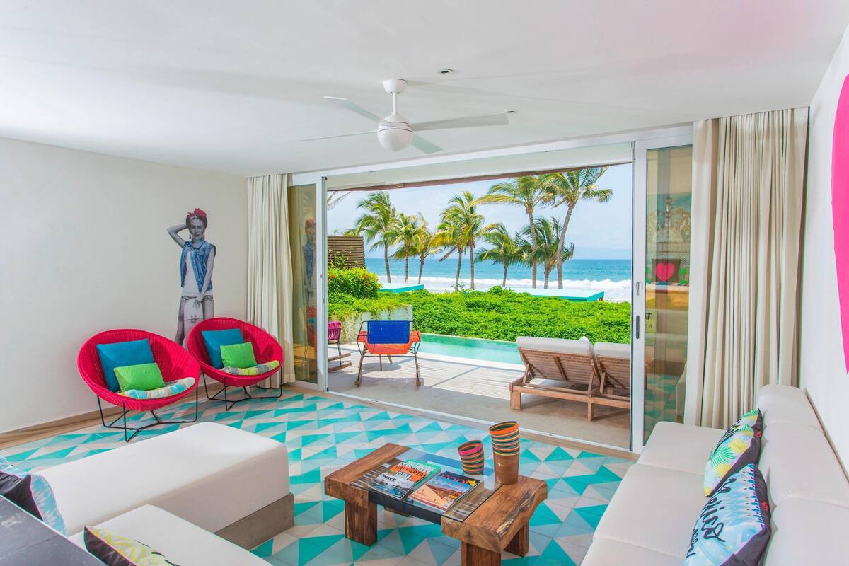 Una habitación con vista al océano, un ventilador de techo, un sofá, dos sillones, una mesa de centro y una puerta de cristal que da a una zona de piscina.