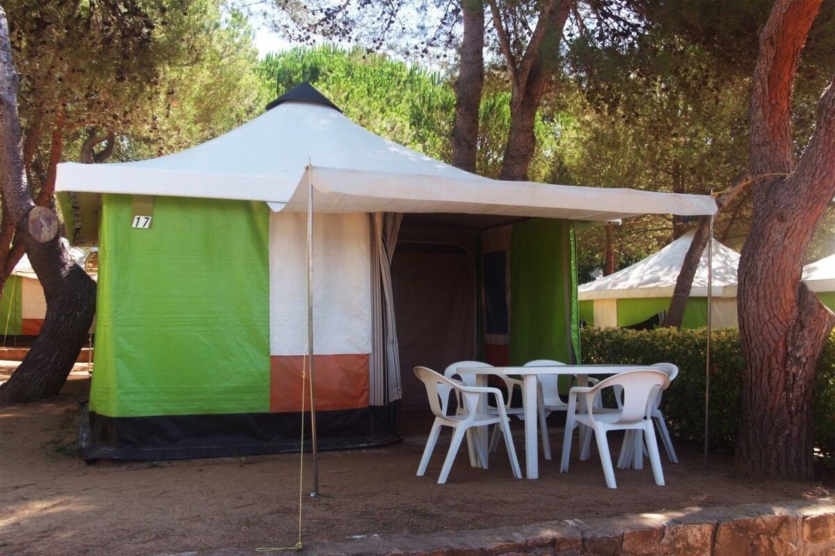 Tenda montada ao ar livre com mesa e cadeiras, cercada por árvores.