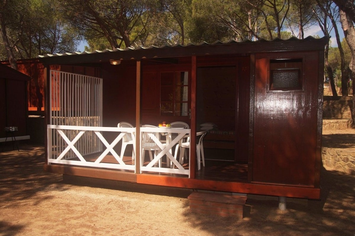 Uma pequena cabana de madeira com corrimão branco, uma mesa e cadeiras.