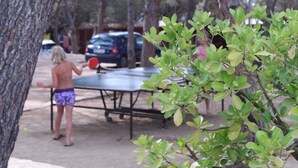 A person playing ping pong outdoors with a table and a car in the background. - Camping Internacional Palamos (Palamós)