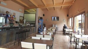 A restaurant with wooden ceiling beams, a bar area with stools, and tables with chairs. - Camping Internacional Palamos (Palamós)
