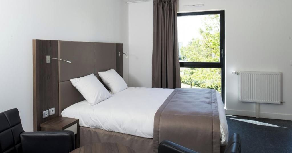 Habitación de hotel con cama, escritorio, silla, ventana con cortinas y radiador.