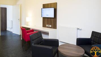 Una habitación de hotel moderna con un escritorio, dos sillones negros, una silla roja y un televisor montado en la pared.
