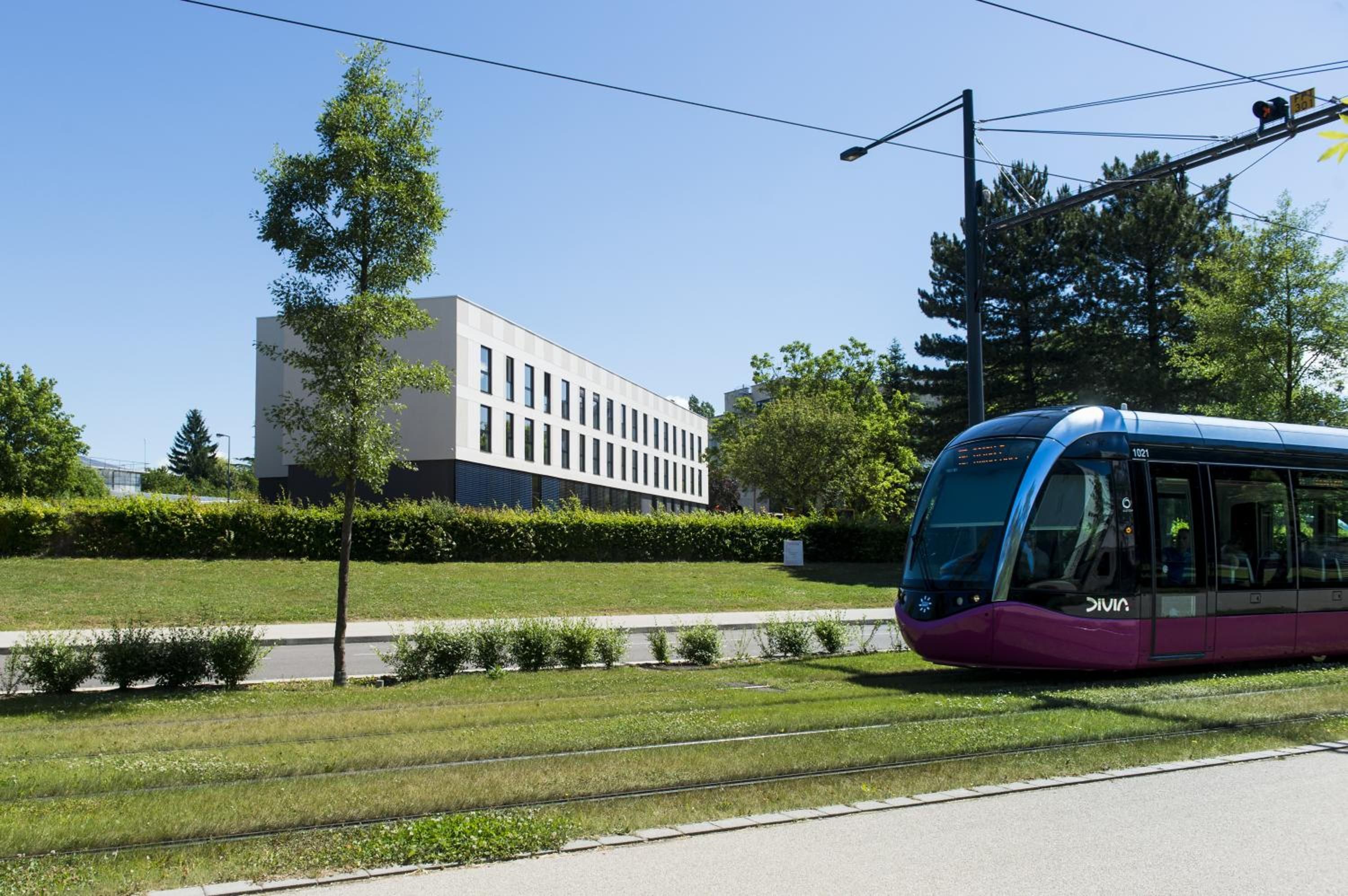 A modern train station with a sleek purple train, a clear sky, and a building with large windows in the background.