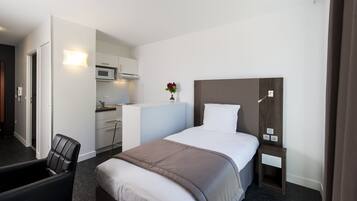 A hotel room with a bed, a desk, a chair, a microwave, and a small plant.