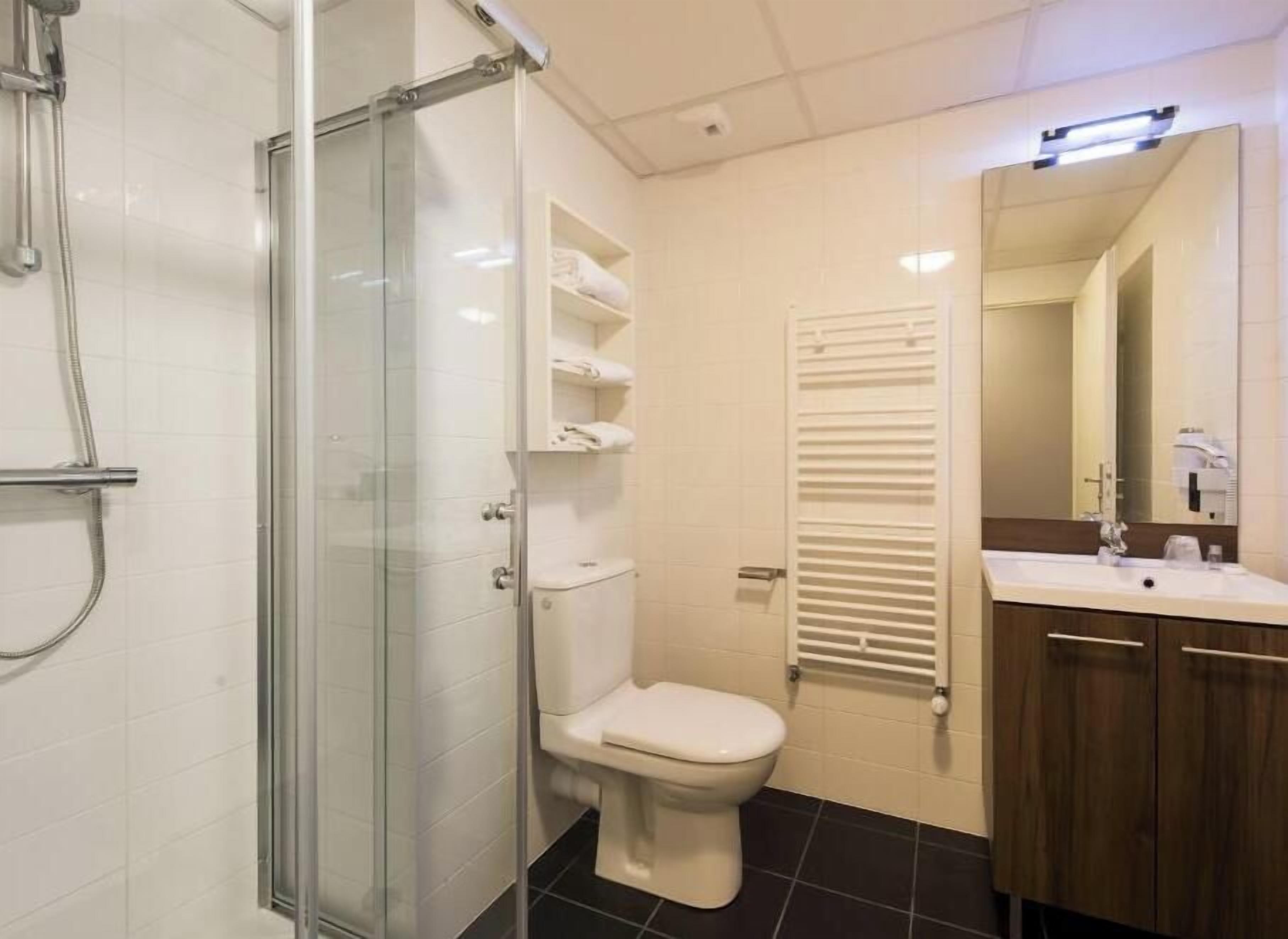 A bathroom with a glass shower enclosure, a toilet, a towel rack, and a sink with a mirror.