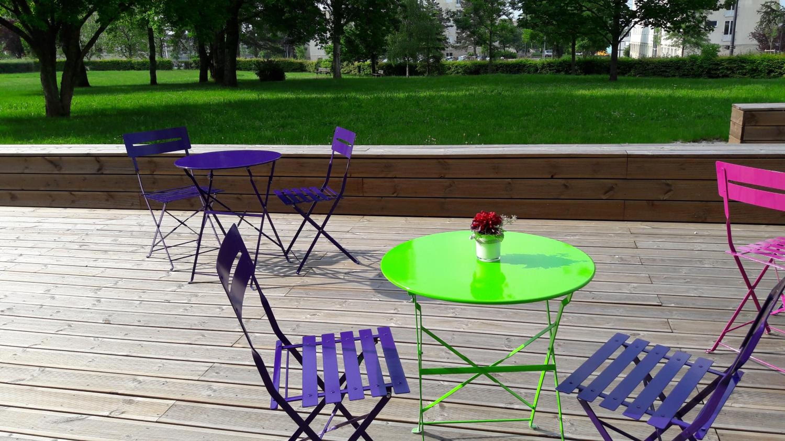 An outdoor seating area with foldable chairs and a table, surrounded by a wooden deck and a grassy park in the background.