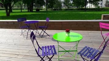 An outdoor seating area with foldable chairs and a table, surrounded by a wooden deck and a grassy park in the background.