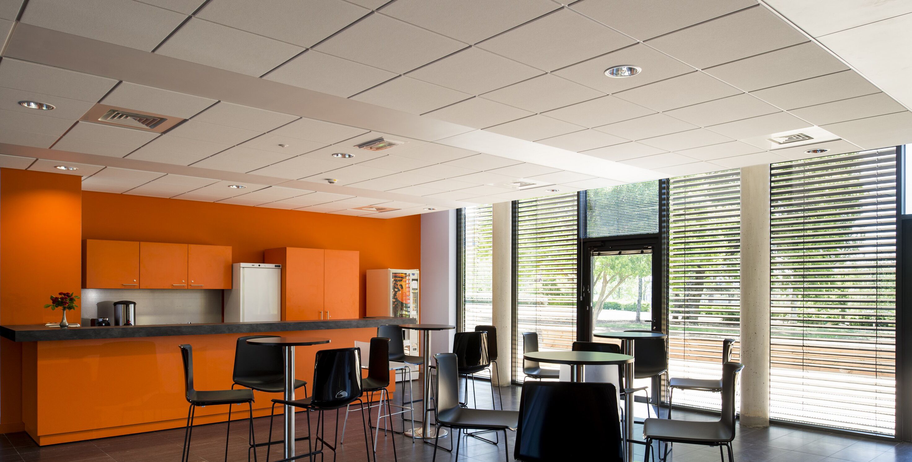 Un espace cuisine moderne avec des meubles orange, un plan de travail noir et des tabourets de bar.