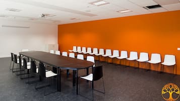 Ett konferensrum med ett långt bord och flera stolar, vita väggar och en orange accentvägg.