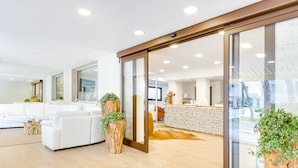 A modern office space with a reception area, white sofas, wooden flooring, and large windows. - Hotel Bellariva (Jesolo)