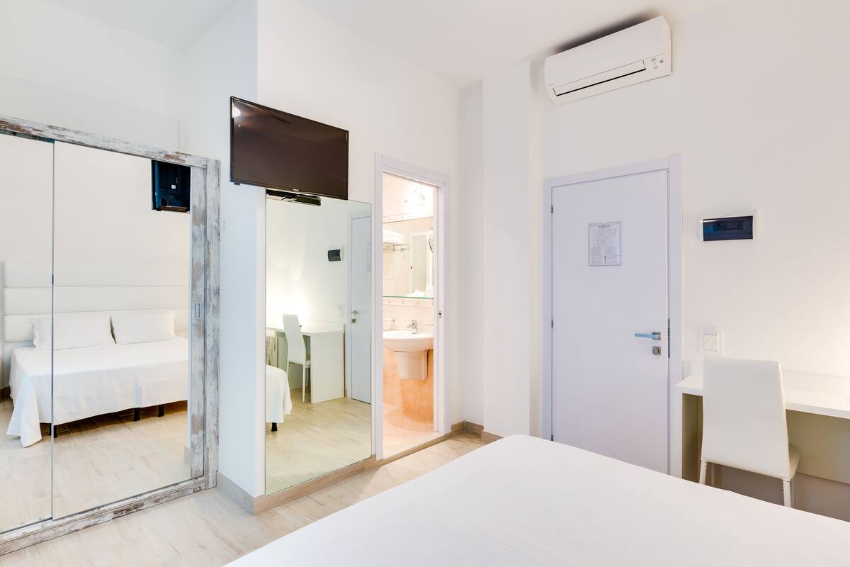 A modern hotel room with a large bed, a desk, and a bathroom visible through an open door.