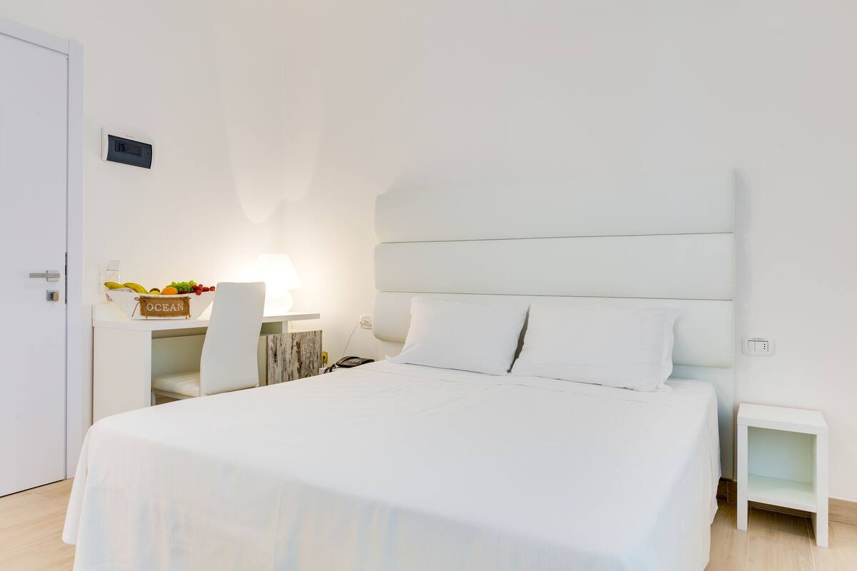 A neatly arranged hotel room with a large bed, a bedside table, a chair, and a small side table.