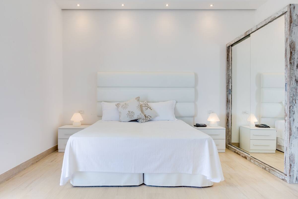 A modern bedroom with a large bed, bedside tables, and a mirror.